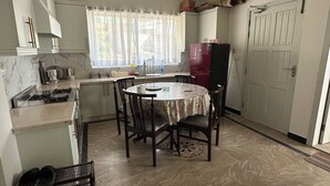 A compact kitchen with a dining table, a refrigerator, and a window with curtains.