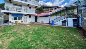 A multi-story residential building with a balcony, a covered patio, and a grassy yard.