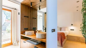 Ein modernes Badezimmer mit Holzwaschtisch, zwei Waschbecken, einem großen Spiegel und einem Bett mit Nachttisch.