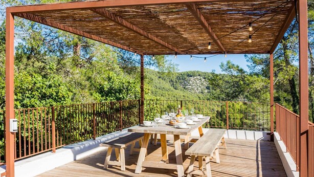 Eine Holzterrasse im Freien mit Esstisch, umgeben von einem Metallzaun und einer Pergola mit Lichterketten.