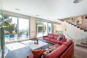 Ein modernes Wohnzimmer mit einem roten Sofa, einem Couchtisch und einer Glastür zum Poolbereich.