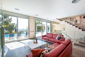 Un salon moderne avec un canapé rouge, une table basse et une porte vitrée donnant sur un espace piscine.