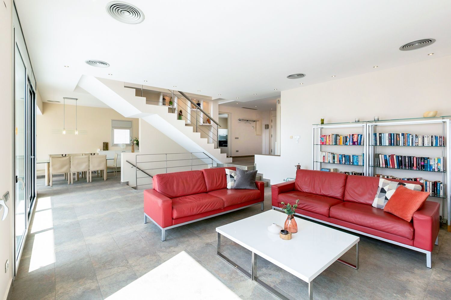 Een moderne woonkamer met rode banken, een witte salontafel en een trap naar een ander niveau.