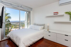 A bedroom with a large window, a bed, a bedside table with a lamp, a shelf with books, and a potted plant. - Villa Havana - Five Bedroom Villa, Sleeps 12 (Quint Mar)
