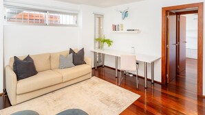 En moderne stue med en beige sofa, et lille bord, en stol, trægulv og en dør.