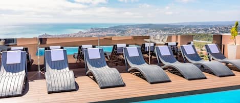 A rooftop pool with lounge chairs and a city view.