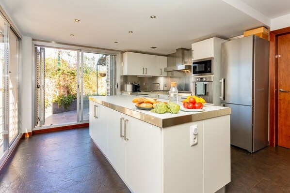 A modern kitchen with a central island, stainless steel appliances, and a sliding glass door leading to a garden. - Villa Havana - Five Bedroom Villa, Sleeps 12 (Quint Mar)
