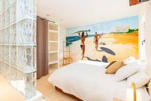 Ein Schlafzimmer mit Bett, Stuhl, Regaleinheit und einem Wandbild mit Strandmotiv.