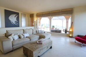 Ein Wohnzimmer mit einem beigen Sofa, einem Holztisch, einem roten Sessel und einem großen Fenster mit Blick.