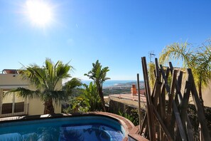 Ein Schwimmbad mit Blick auf das Meer und die Berge, umgeben von tropischer Vegetation und einem Holzzaun.