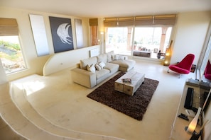 Ein modernes Wohnzimmer mit einer Couch, einem Couchtisch und einem roten Sessel. An den Wänden befinden sich Kunstwerke und ein Fenster mit Blick.