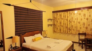 Une chambre à coucher comprenant un lit, des tables de chevet, une chaise, une lampe, des rideaux et une étagère fixée au mur.