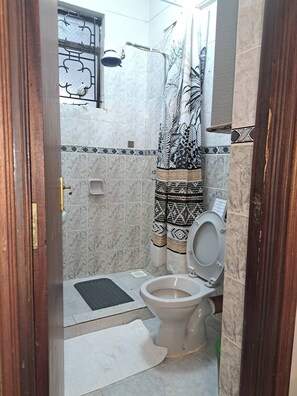 Ein kleines Badezimmer mit Toilette, Dusche und einem gemusterten Vorhang.