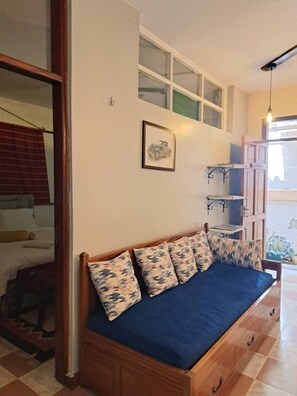 Una habitación con sofá cama de madera, un cuadro enmarcado en la pared y una ventana con persianas.
