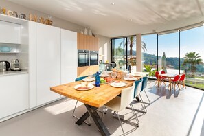 Eine moderne Küche mit weißen Schränken, einem Holztisch und Blick ins Freie.