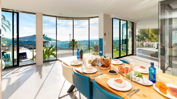 Zona pranzo con vista panoramica, un tavolo in legno apparecchiato con piatti, bicchieri e bottiglie, e sedie blu.
