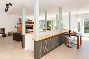 Una cocina moderna con encimera de madera, una zona de comedor con mesa y sillas, y un televisor en un estante.