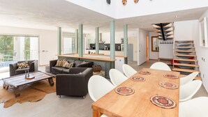 Et moderne opholdsrum med spiseplads, sofaer, et sofabord og en trappe.