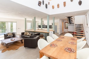 Un espacio habitable moderno con comedor, sofás, una mesa de centro y una escalera.