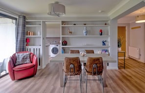 A modern kitchen with a dining area, a red chair, and a large window.