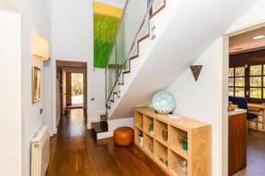 Ein modernes Interieur mit Holzboden, einer Treppe, einem Bücherregal und Blick durch ein Fenster.