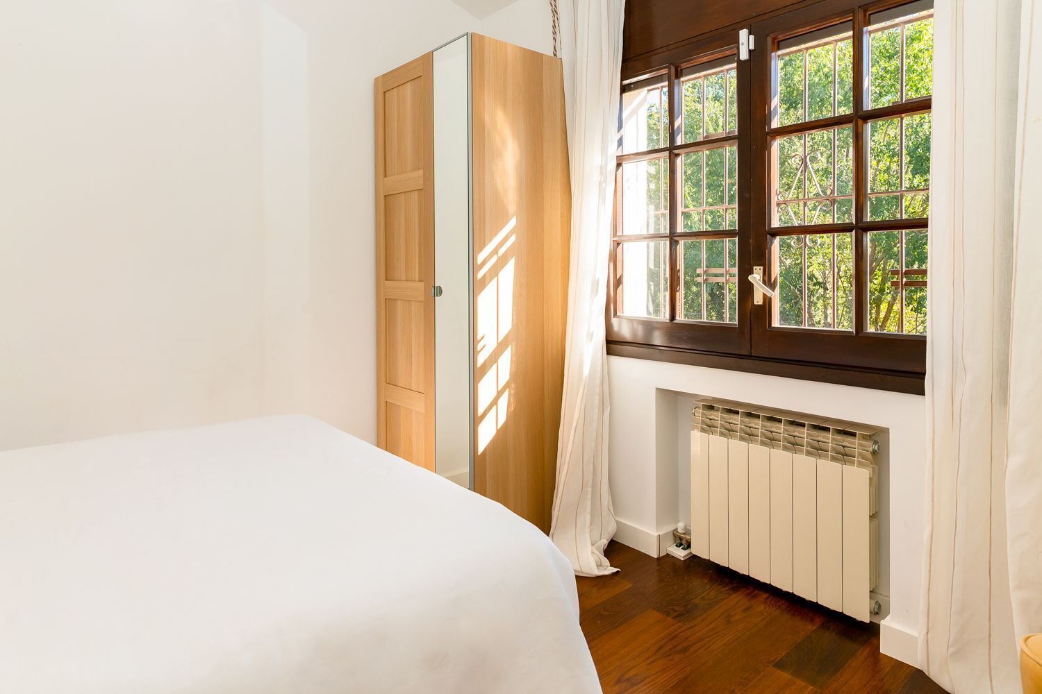 A bedroom with a bed, a wardrobe, a radiator, and a window with curtains.