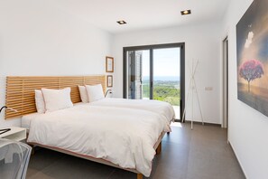 Ein Schlafzimmer mit einem großen Bett, einem Holzkopfende, Blick durch eine Schiebetür und einem Bild an der Wand.