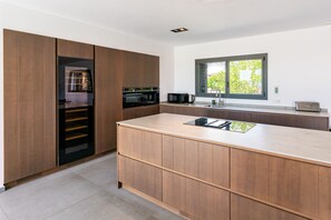 Ett modernt kök med träskåp, en inbyggd ugn, en mikrovågsugn och ett fönster med utsikt över grönområden.