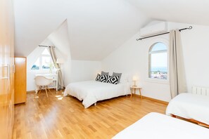 Ein Schlafzimmer mit einem Bett, einem Schreibtisch und einem Sessel. Ein Fenster bietet Blick auf das Meer.