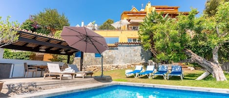 Une piscine avec des chaises longues, une pergola dotée d’un parasol et un mur en pierre.