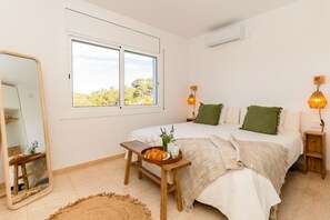 Ein Schlafzimmer mit Bett, Nachttischlampen, einem Nachttisch mit Essensserviertablett, einem Spiegel und einem Fenster mit Blick auf Grünflächen.