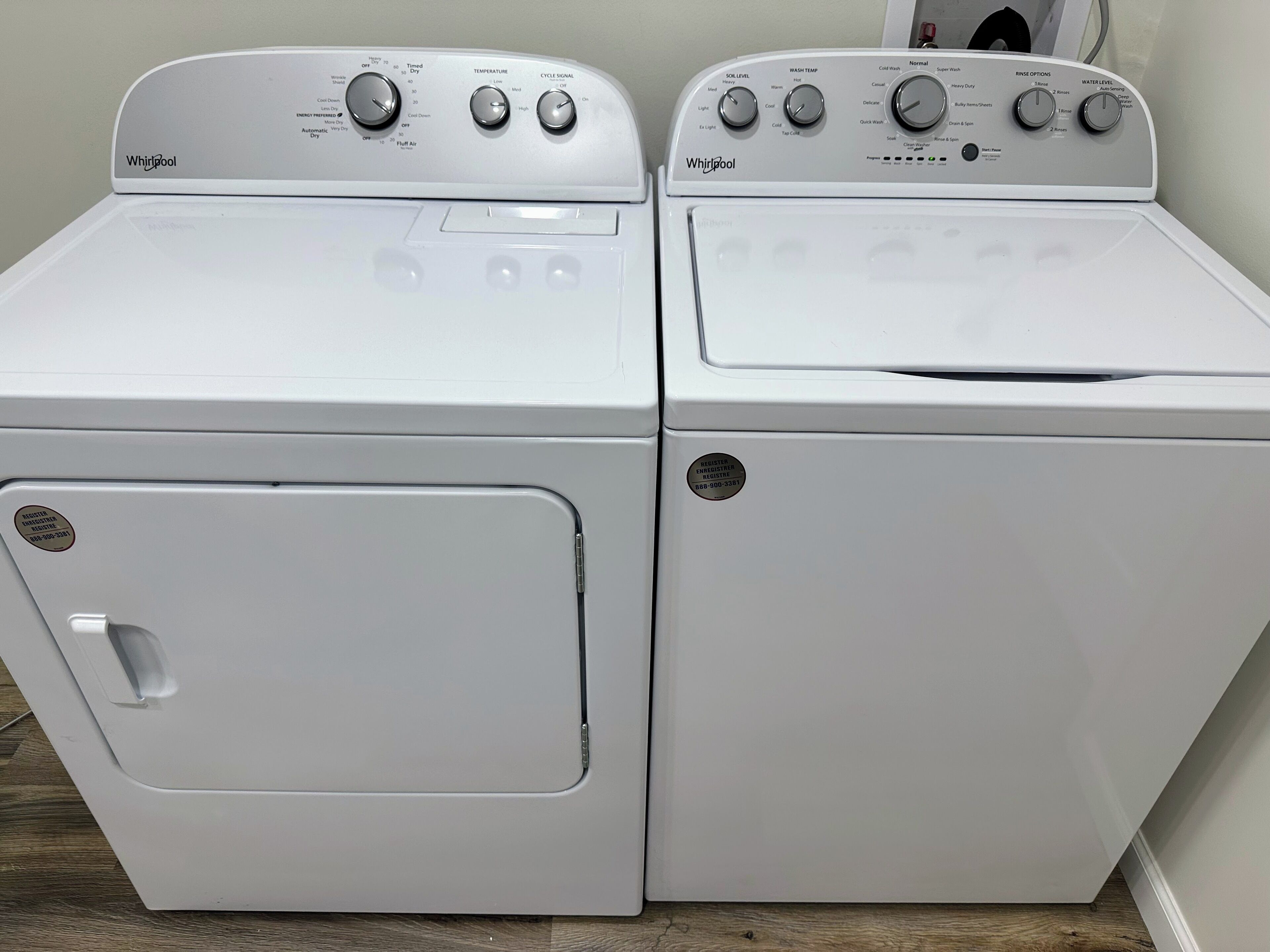 Zwei weiße Whirlpool Waschmaschinen mit Frontlader, Bedienfeldern, Türgriffen und einem Aufkleber mit einer Telefonnummer.