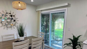 A dining area with a wooden table, chairs, a potted plant, a decorative wall piece, and a sliding glass door leading to a patio. - Charming 2BR Cottage - Short walk to Missouri Star & Downtown Hamilton (Hamilton)