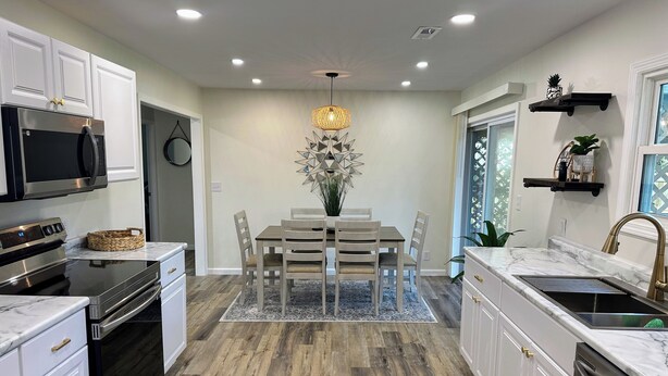 A modern kitchen with white cabinetry, a central island, and a dining area with chairs and a chandelier. - Charming 2BR Cottage - Short walk to Missouri Star & Downtown Hamilton (Hamilton)