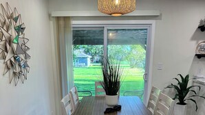 A dining area with a wooden table, white chairs, a hanging light fixture, and a view through a glass door. - Charming 2BR Cottage - Short walk to Missouri Star & Downtown Hamilton (Hamilton)