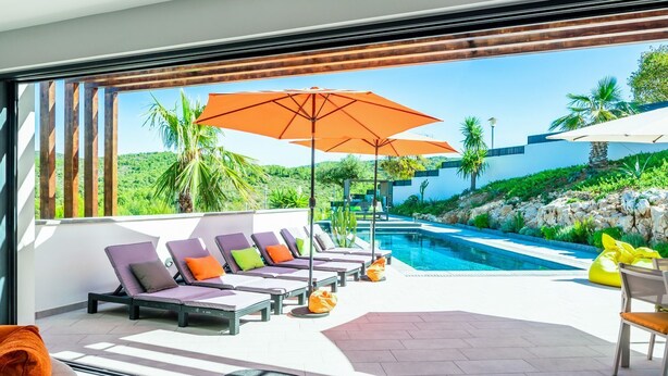 Un espace piscine extérieur moderne, doté de chaises longues et de parasols, entouré de verdure et offrant une vue dégagée sur le paysage.
