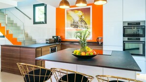Une cuisine moderne dotée d’un îlot central, d’appareils électroménagers en acier inoxydable et d’un escalier agrémenté de touches de couleur orange.