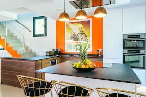 Eine moderne Küche mit einer zentralen Kochinsel, Edelstahlgeräten und einer Treppe mit orangefarbenen Akzenten.