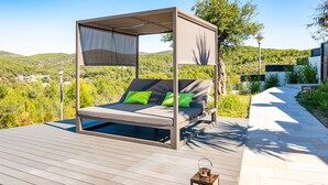 Un lit d’extérieur moderne, doté d’un auvent, de coussins verts et offrant une vue sur un paysage luxuriant.