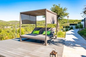 Ein modernes Outdoorbett mit Baldachin, grünen Kissen und Blick auf eine üppige Landschaft.