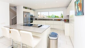A modern kitchen with a central island, white cabinetry, stainless steel appliances, and a view through large windows.