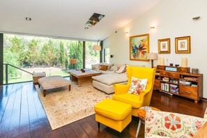 Ein modernes Wohnzimmer mit einer Couch, einem Sessel, einem Hocker, einem Holztisch und einem Bücherregal.