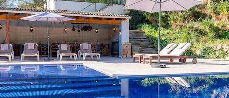 A modern outdoor pool area with lounge chairs and a barbecue setup.