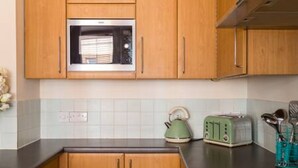 Uma cozinha com armários de madeira, micro-ondas, chaleira verde e torradeira de estilo vintage.