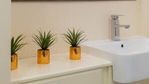 Um banheiro com uma pia branca, um espelho e três pequenas plantas em vasos sobre o balcão.