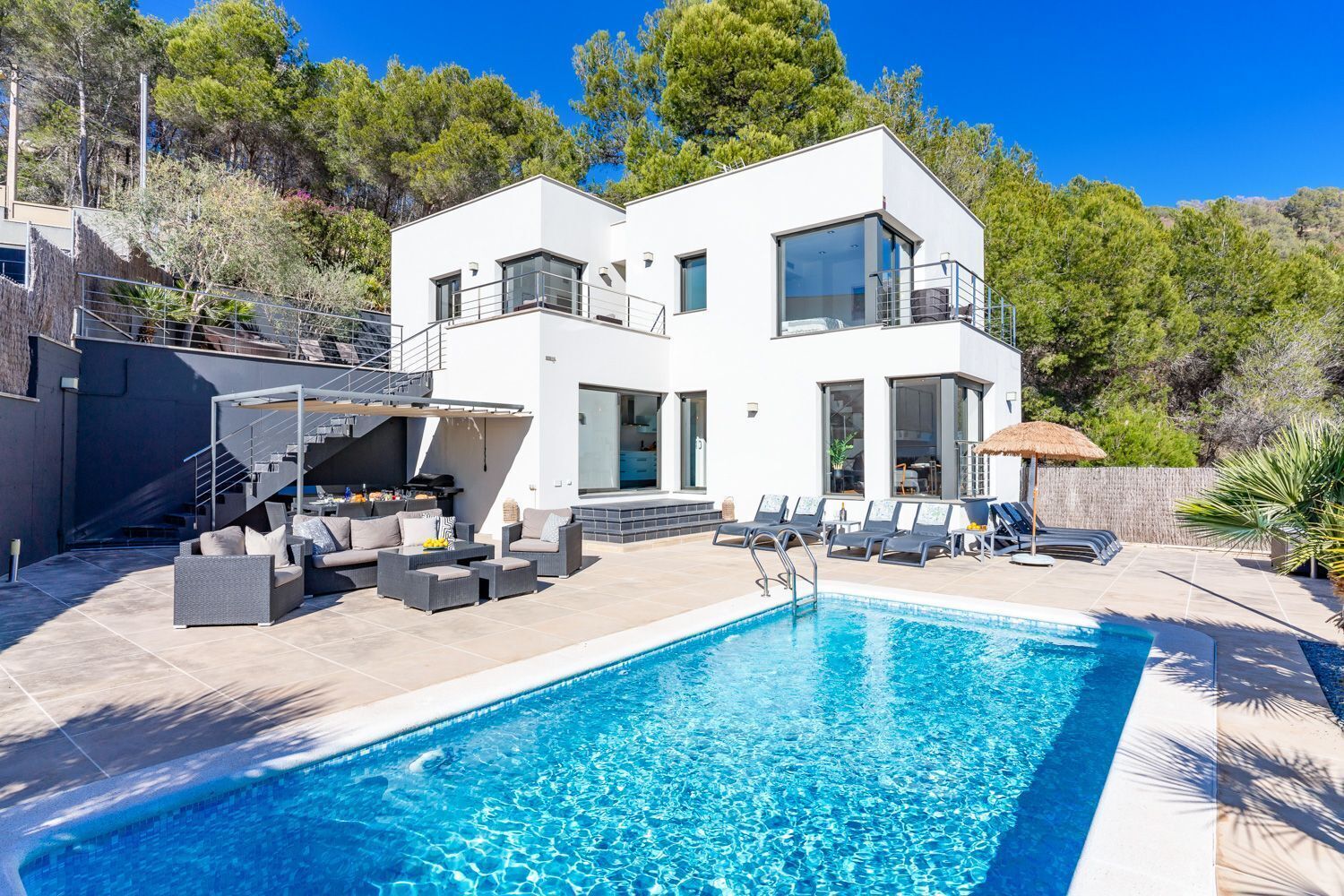 A modern two-story house with a swimming pool, outdoor seating, and a staircase leading to a deck.