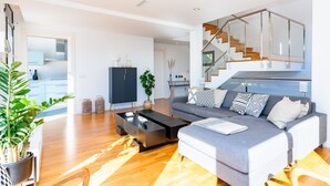 Ein modernes Wohnzimmer mit grauem Sofa, einem schwarzen Couchtisch und einer Treppe mit Glasgeländern.