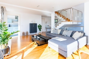 Ein modernes Wohnzimmer mit grauem Sofa, einem schwarzen Couchtisch und einer Treppe mit Glasgeländern.