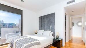 Ein modernes Schlafzimmer mit einem großen Bett, zwei Nachttischen, einer grauen Akzentwand und Blick durch ein großes Fenster.
