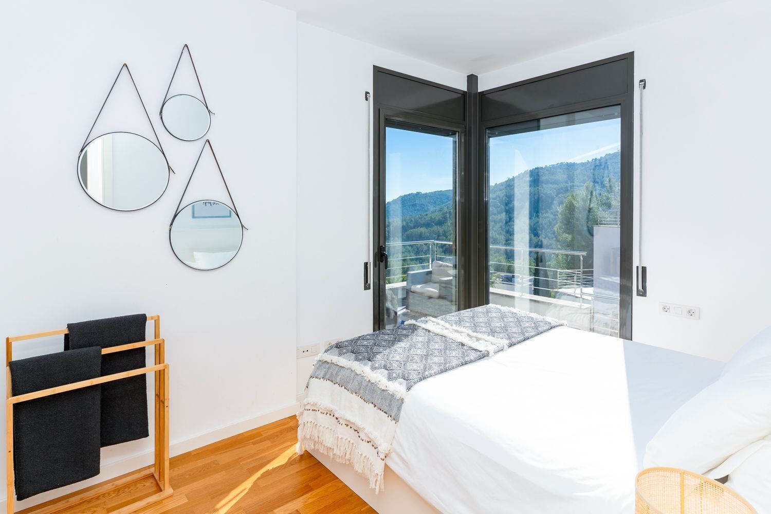 A bedroom with a bed, a wooden towel rack, and a balcony with a view of the mountains.